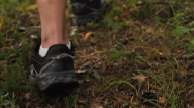 Bir insan çimen ve sopalarla kaplı bir şekilde ormanda yürür. Orman zeminine ayak basan ayak izleriyle doğayı keşfediyor..