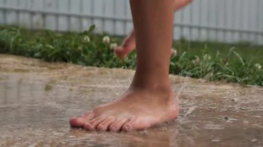 Genç çocuk yağmurda çıplak ayakla oynamanın ve dans etmenin zevkini yaşıyor. Etrafı taze yeşillik ve damlacıklarla çevrili. Doğal bir neşe anı yakalıyor.