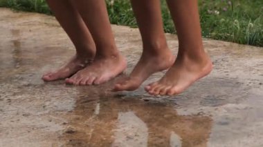 İki çocuk, arka bahçedeki beton bir yüzey üzerinde çıplak ayakla zıplamaktan ve su birikintilerinde oynamaktan zevk alır..