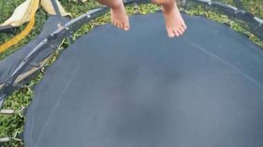 Neşeli küçük bir çocuk bahçedeki trambolinde çıplak ayakla zıplıyor güneşli bir yaz gününün tadını çıkarıyor..