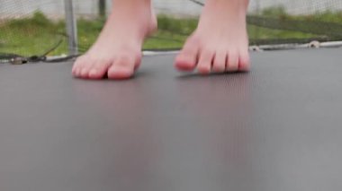 Arka bahçede trambolinde çıplak ayakla zıplayan ve güneşli bir yaz gününün tadını çıkaran çocuk ayaklarının yakın plan çekimi..