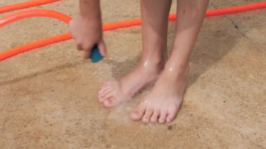 Çocuk arka bahçede bahçe hortumuyla ayaklarını yıkıyor sıcak ve güneşli bir günde ferahlatıcı suyun tadını çıkarıyor. Sahne çocukluk sevincini ve basit yaz eğlencesini yakalar..