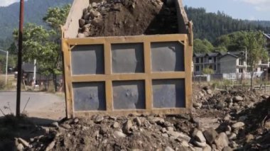 Büyük bir çöp kamyonu inşaat alanının yanına toprak bırakıyor. Ağır çöp kamyonu yerleşim alanının yakınındaki kayalık zemini boşaltıyor..