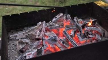 Bir kişi ızgarada odun ateşini maşayla ustalıkla düzenliyor. Bir yaz öğleden sonrasında bahçede ızgarada barbekü yangını hazırlıyorum..