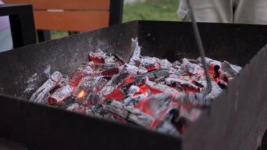 Bir kişi ızgarada odun ateşini maşayla ustalıkla düzenliyor. Bir yaz öğleden sonrasında bahçede ızgarada barbekü yangını hazırlıyorum..