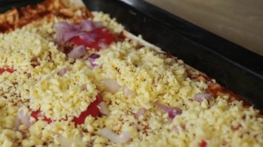 Metal yemek tepsisinde taze domates, soğan ve peynir soslu lezzetli bir ev yapımı pizza hazırlıyorum..