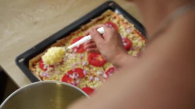 Bir ev hanımı mutfak masasına lezzetli bir ev yapımı pizza yapar. Taze domates dilimleri ve peynir malzemelerini yemek tepsisinin üzerine koyar..