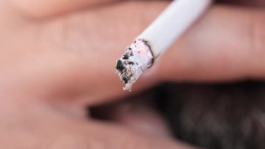 Yanan bir sigara çubuğunun yakın çekimi. Bir insan sigara çubuğu tutup sigara içiyor..