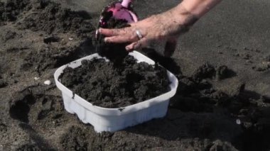 Yaz eğlencesi sırasında plajdaki kumla plastik bir kalıbı eller doldurur..
