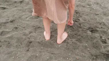 Bir kadın kumsalın tadını çıkarır ve tahıllarla oynar. Sıcak bir kumsalda, bej elbiseli, eli kumsalda, hafif bir esinti sırasında oynayan beyaz bir kadının yakın çekimi..