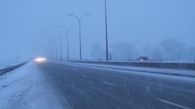 Şiddetli kış şartları altında, trafik ışıkları açık ve karlı otoyolda giden arabalar görülüyor. Otoyolda kar fırtınası sırasında araba trafiği.