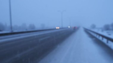 Karlı bir otoyolda gün batımında sınırlı görüş mesafesi olan arabaların bulanık videosu. Akşamki kış fırtınası sırasında arabalar uzun yolda yol alıyorlar. Karlar yağarken otoyolda koşuşturan arabalar.
