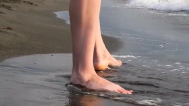 Çıplak kadınsı bacaklar ıslak kumlu sahil şeridinde geziniyor, sakin sahil anında hafif su okşayışı ve ritmik okyanus dalgaları yaşıyor.