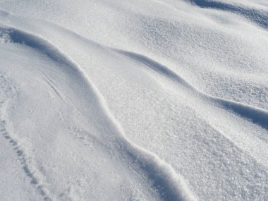 Parlak kar yığınları el değmemiş kar yüzeyinde dalgalı desenler oluşturuyor..