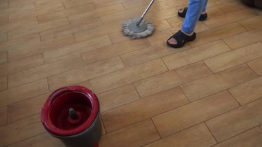 Profesyonel temizlik profesyoneli paspas ve kova kullanarak döşeme döşeme yüzeyini temizliyor. Ev bakımını ve hijyenik temizlik tekniğini gösteriyor.