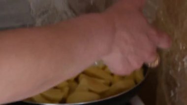 Patatesleri konteynırdan cızırdayan tavaya dökerek gaz ocağının üstüne oturarak.