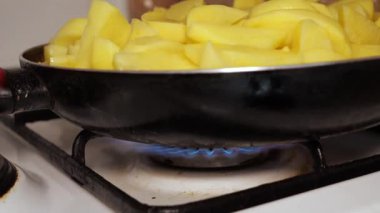Gaz ocağında siyah bir tavada yağda kızaran patates dilimleri.