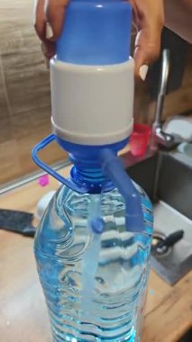 Kadınların elleri büyük plastik bir şişenin üzerinde elle su pompası düzenliyor.