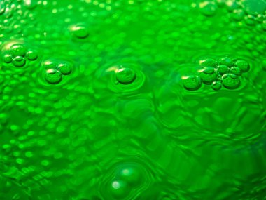 Yeşil kabarcıklı sıvı yüzey eşmerkezli daireler oluşturuyor ve ışığı yansıtıyor