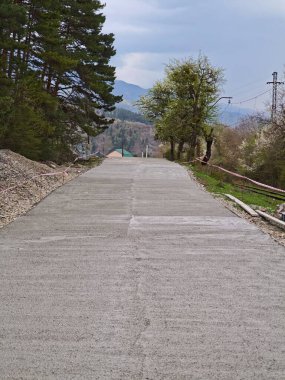 Yeni inşa edilmiş beton yol, bulutlu bir gökyüzünün altındaki uzak dağlara doğru uzanıyor.