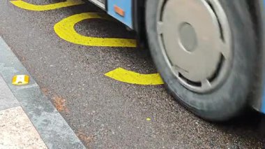 Sarı bir otobüs durağından geçen toplu taşıma otobüsleri sokakta yazıyor.