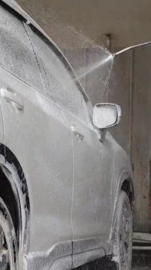 Bir oto yıkama garajında yıkanırken gri, modern bir arabayı kaplayan aktif köpük.