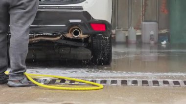 Profesyonel oto yıkama çalışanı beyaz cipin arkasını temizlemek için basınç makinası kullanıyor.