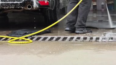 Araba yıkama çalışanı araba paspasına yüksek basınçlı su püskürtüyor.
