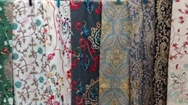 Bir tekstil dükkanında çeşitli desenlere ve renklere sahip işlemeli kumaşlar asılı.