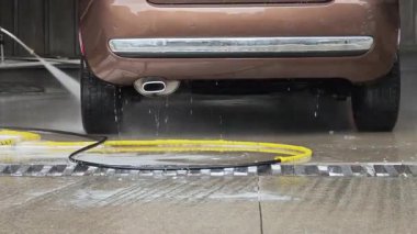 Araba yıkama çalışanı kahverengi arabanın arkasını temizlemek için basınç makinası kullanıyor.