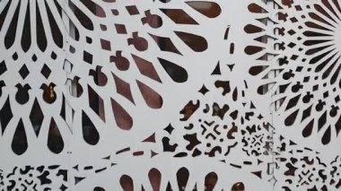 Karmaşık beyaz dekoratif paneller, dairesel ve çiçek desenli, yavaşça sallanarak büyüleyici bir görsel etki yaratıyor.