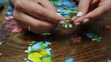 Kadın, ahşap bir masada renkli yapboz parçalarına katılıyor, rahatlatıcı bir meşgale ile meşgul oluyor.