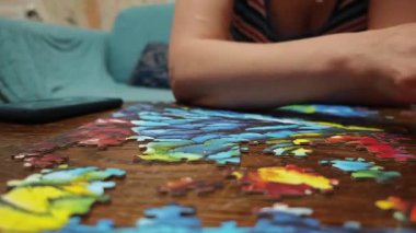 Tahta bir masada yapboz hazırlayan kadın parçaları toplayıp yerleştiriyor.