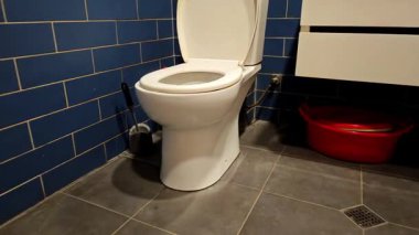 Modern mavi fayanslı banyoda beyaz klozet kapağı yavaşça kapanıyor.