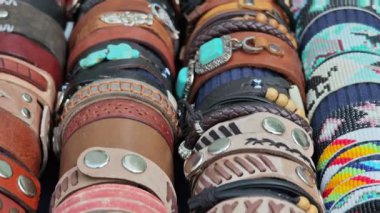 Piyasada turkuaz taşlar ve metal süslemeler içeren deri ve boncuklu bilezikler sergileniyor.