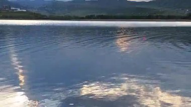 Gökyüzünde hareket eden güzel bulutlar, gölün sakin sularında yansıyor.