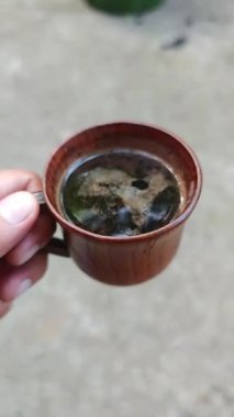 Elinizde gökyüzü ve ağaç yansımalı ahşap kahve fincanı, dingin bir sabah anı ve doğal kahve deneyimi.