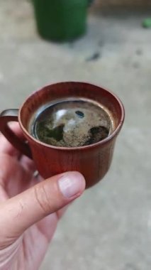 Elinde koyu, aromatik bir kahve olan tahta bardak, kırsal detayları vurguluyor ve sıcak bir sabah uykusunda dinleniyor.