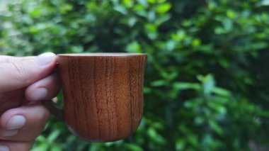 Canlı yeşil yapraklarla çevrili kırsal ahşap kahve fincanı, organik içecek estetiği ile doğal sabah anlarını yakalıyor.