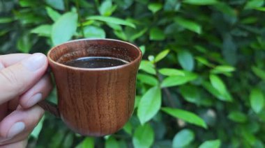 Canlı yeşil yapraklarla çevrili kırsal ahşap kahve fincanı, organik içecek estetiği ile doğal sabah anlarını yakalıyor.