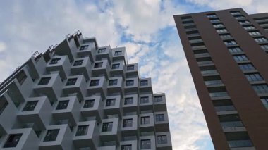 Modern mimari yapılar bulutlu ufuk çizgisine karşı yükseliyor, çağdaş şehir manzarasını yakalayan kendine özgü şehir tasarım elemanlarıyla gösterişli geometrik cepheler sergiliyor.