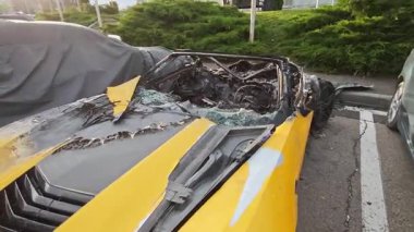 Şiddetli hasarlı sarı spor araba geniş çaplı yangın kaynaklı yıkım taşıyor. Açık hava otoparkında ceset ve iç organları çıkarılmış.