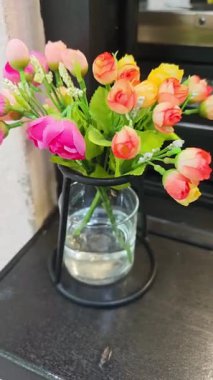 Çağdaş siyah metal bir vazoya yerleştirilmiş canlı yapay güller, pencere pervazına biraz renk katıyor.