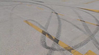 Gri asfalt boyunca uzanan fren izleri, kesişen sarı çizgiler, yüksek hız otomotiv performansının dinamik hareketlerini gösteriyor.