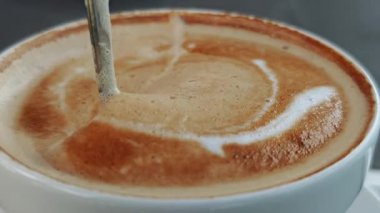 Profesyonel barista karmaşık latte sanatı yaratırken buğulanmış sütü dikkatlice taze demlenmiş espressoya dökerek zengin kahverengi yüzey üzerinde hassas beyaz desenler oluşturuyor.