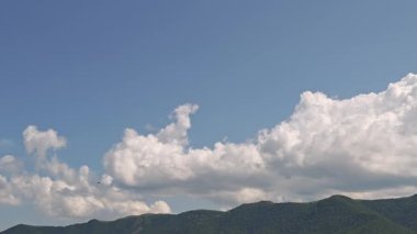 El değmemiş beyaz kümülüs bulutları hareketli mavi yaz gökyüzü altında yeşil tepelerin üzerinde sürükleniyor ve şekil değiştiriyor.