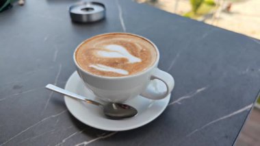 Koyu mermer bir masada, kaşık ve şeker paketleriyle servis edilen altı bardak kapuçino.