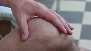 Travma ya da spor yaralanmasından sonra dizine masaj yapan bir adam.