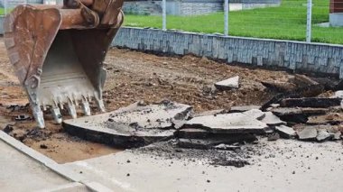 Kazıcı, modern evlerin yakınındaki yol onarım çalışmaları sırasında asfalt enkazını kaldırır ve bir çöp konteynırına yükler.