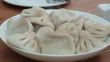 Baharatlı etle dolu Gürcistan hamur tatlısı Khinkali, bir tabakta servis edilir ve bir tanesi çatalla alınır.